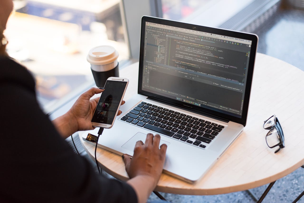 Desenvolvimento Web na Prática: A Importância da Mobilidade e Multitarefas 3 Developer working remotely, coding on a laptop with phone in hand, showcasing modern work culture.